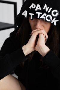 Close-up of a person in a hoodie with 'panic attack' text, hands to face.